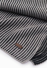 Coperta lavorata a maglia con strisce grigie e nere, caratterizzata da una texture liscia e da una piccola etichetta con logo marrone. I bordi sono rifiniti con cura.