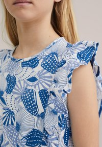 Mėlynas ir baltas be rankovių viršus su kriauklės ir augalų raštu, raukiniais ir švelnia medvilnės tekstūra.