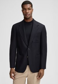 Granatowa marynarka ze strukturalnej tkaniny, z dwoma przednimi kieszeniami, kołnierzem z klapami i dwoma guzikami. Nosi się ją na czarnym golfie.