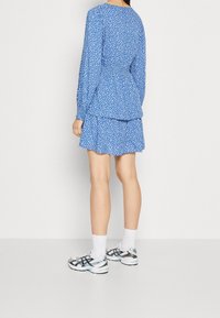 Robe bleue à pois blancs, manches longues et jupe à volants. Associée à des chaussettes blanches et des chaussures de sport multicolores.