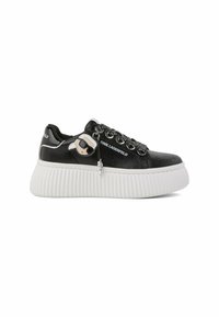 Sneakers basses en cuir noir avec semelle blanche épaisse côtelée, logo Karl Lagerfeld et breloque décorative sur les lacets noirs.