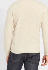 Beige stickad tröja med rund halsringning, långa ärmar och ribbade muddar. Tyget har en mjuk känsla och en slät yta.