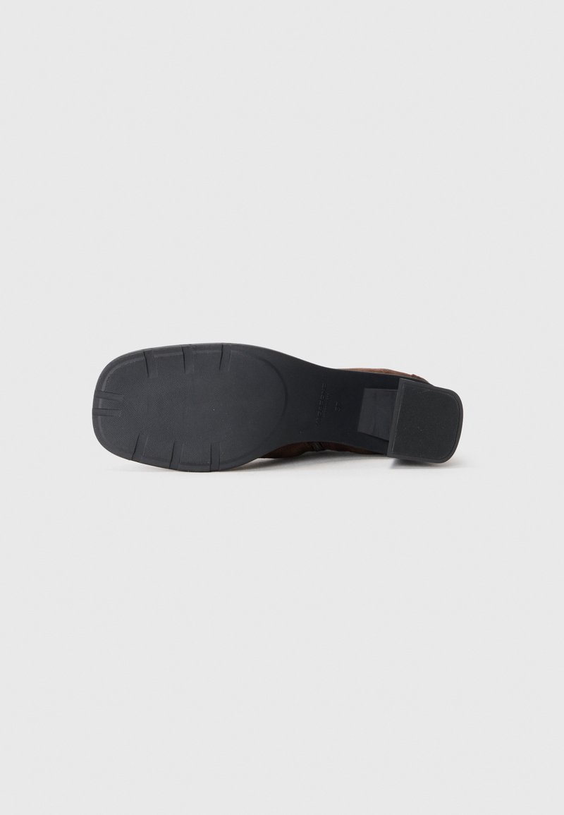 Chaussure à talon en cuir suédé marron avec une semelle extérieure en caoutchouc noir lisse. Présente un bout arrondi et un talon bas en bloc. Détails texturés sur la tige.