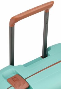 Turkis farge koffert med en teksturert overflate, som har et brunt plastikkhåndtak og en grå metallramme, inkludert en låsbar spenne.