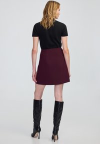 Een aansluitend zwart topje gecombineerd met een bordeauxrode rok, met een gladde textuur en een uitlopende zoom. Tot de knie hoge zwarte leren laarzen met stilettohakken.