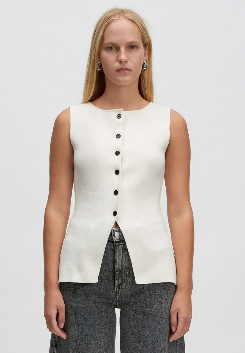 Cremefarbener, ärmelloser Oberteil mit rundem Halsausschnitt, ausgestattet mit einer sechs Knöpfe langen Knopfleiste auf der Vorderseite und einem gespaltenen Saumdesign. Weicher, strukturierter Stoff.