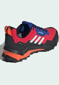 Punainen ja musta vaelluskengä, jossa on sininen ja oranssi kantapääkorostus. Varustettu kolmella valkoisella raidalla, teksturoidulla pinnalla ja karkealla pohjalla.