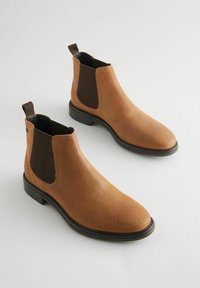 Botas Chelsea de cuero marrón con paneles elásticos en los costados, puntera redondeada y tirador; superficie texturizada y suela de goma negra.
