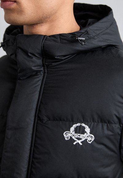 Sort pufferjakke med høj krave, har et quiltet design, snorede detaljer og et hvidt broderet Moschino-logo på brystet.