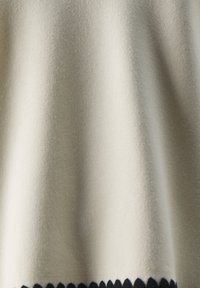 Beiger Pullover mit glatter Textur, der über einen schwarzen gewellten Saum verfügt. Das Design ist einfach und lässig in der Form.