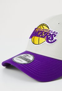 Los Angeles Lakers cap featuring a grey crown, purple visor, and an embroidered logo with a basketball. Adjustable with textured fabric.