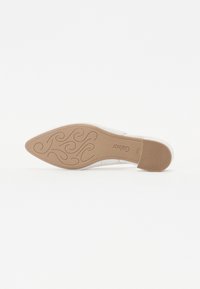 Chaussure blanche avec un bout pointu et une semelle texturée. La marque et des tourbillons décoratifs sont embossés sur la semelle beige. Éléments de design minimalistes.
