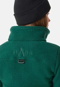 Giacca in pile verde con colletto rialzato, caratterizzata da un logo marchiato e un accento in metallo sul retro. Tessuto morbido e design casual.