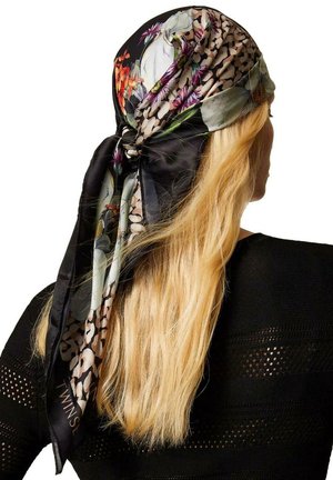 Donna bionda con capelli lunghi che indossa un foulard di seta nero con motivo floreale annodato dietro, vestita con un maglione nero lavorato a maglia.