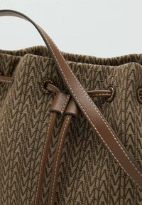 Sac seau en textile marron avec un motif en zigzag, doté d'une fermeture à cordon, d'accents en cuir et d'une longue bandoulière.
