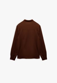 Bruine langslavige shirt gemaakt van een gladde stof. Heeft een eenvoudige kraag, met knopen afsluitbare manchetten en een minimalistisch ontwerp zonder zichtbare patronen.