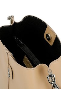 Sac seau en cuir beige avec une finition lisse, intérieur en tissu noir, quincaillerie en argent et poche zippée. Présente une fermeture à pression et des coutures contrastantes.