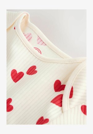 Licht crèmekleurige stof met een geribbelde textuur en rode hartpatronen. Afgewerkt met een zachte, afgeronde halslijn en stikseldetail.