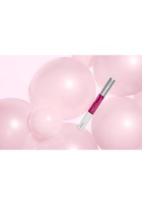 Lippenbehandlungstift mit weißer und pinker Verpackung, schwebend zwischen großen, durchsichtigen rosa Kugeln vor einem hellrosa Hintergrund.