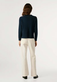 Marineblauwe geribbelde trui met lange mouwen en een ronde hals, gecombineerd met crème wijde broek. Gladde textuur en ontspannen pasvorm.