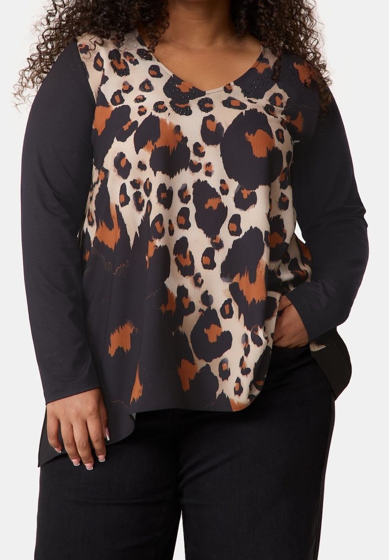 Femme portant un haut à manches longues avec des manches noires et un devant imprimé léopard marron, noir et beige, associé à un pantalon noir.