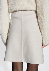 Jupe en laine de couleur crème avec une couture centrale, portée avec un pull en crème pelucheux assorti et des collants noirs transparents.