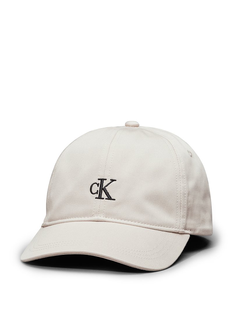 Gorra de algodón beige con visera curva, que presenta un logotipo bordado en negro "ck" en la parte frontal. Textura suave, correa trasera ajustable.