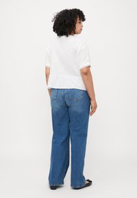 White short-sleeve top with lace trim, paired with blue wide-leg jeans. The outfit features a relaxed fit and lightweight fabric.