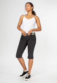 Zwarte cropped cargobroek met opgerolde pijpen, zakdetails en een patroonriem, gecombineerd met een wit tanktop en zwarte sneakers.