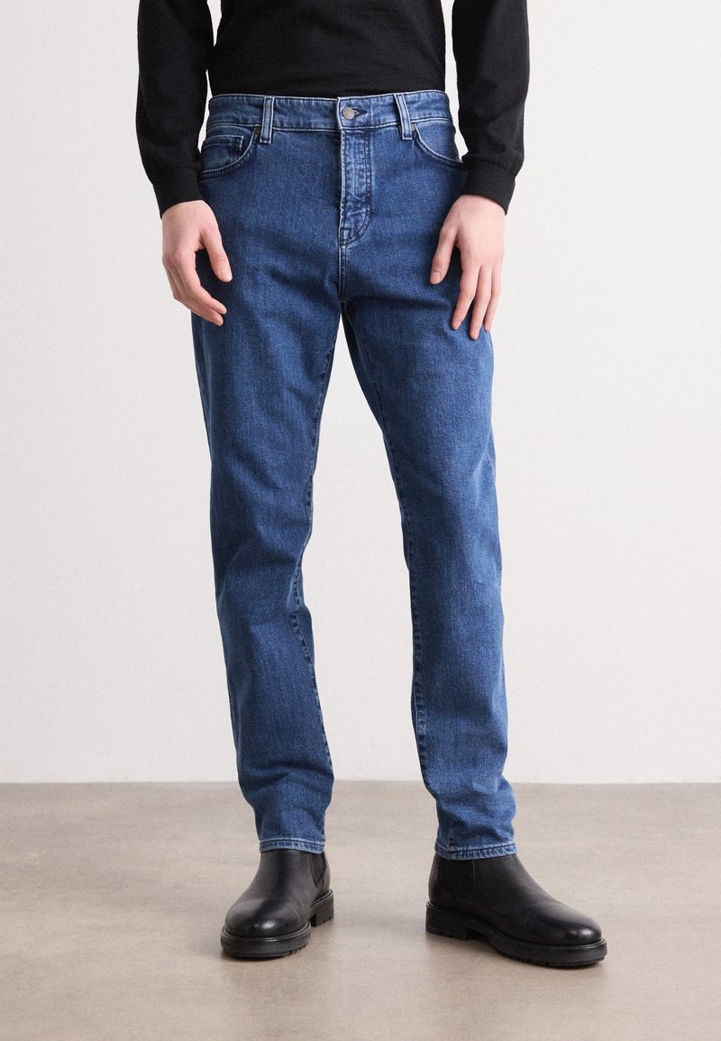 Blue denim jeans with a straight fit, five pockets, and a metal button closure. Worn with black leather ankle boots.