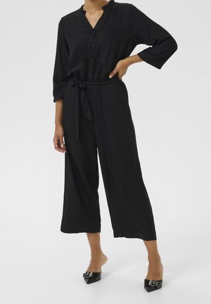 Sort jumpsuit med trekvartlange ærmer, knapper foran og elastisk talje. Har et bundet bælte og bredt ben-design. Glat stoftekstur.