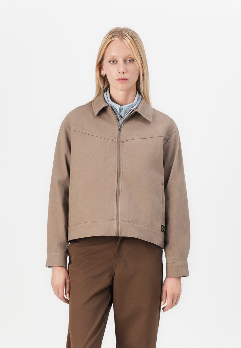 Brown cropped jacket made of thick fabric, featuring a zip front, collar, and two side pockets. Worn over a light blue shirt.