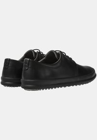 Scarpe in pelle nera con punte arrotondate, design a profilo basso e suole in gomma dotate di grip testurizzato. Lacci e dettagli di finitura liscia.