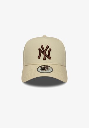Gorra de béisbol beige con un logo NY bordado en marrón. Presenta una corona estructurada, visera curvada y correa ajustable en la parte posterior.