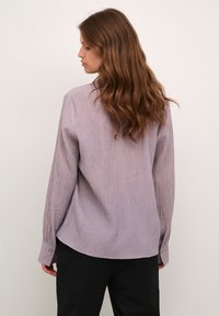 Camicia a righe viola con vestibilità ampia, maniche lunghe e polsini con bottoni, caratterizzata da un orlo curvo e un tessuto testurizzato.