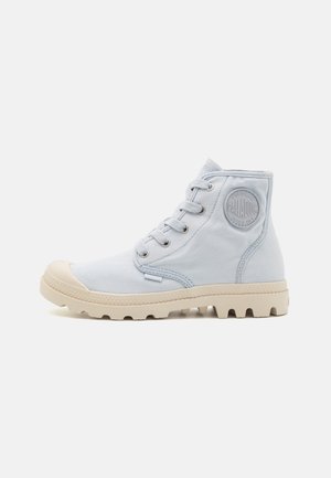 Chaussure montante en toile bleu clair avec bout rond, semelle extérieure en caoutchouc blanche, coutures visibles et patch de logo en relief sur le côté.