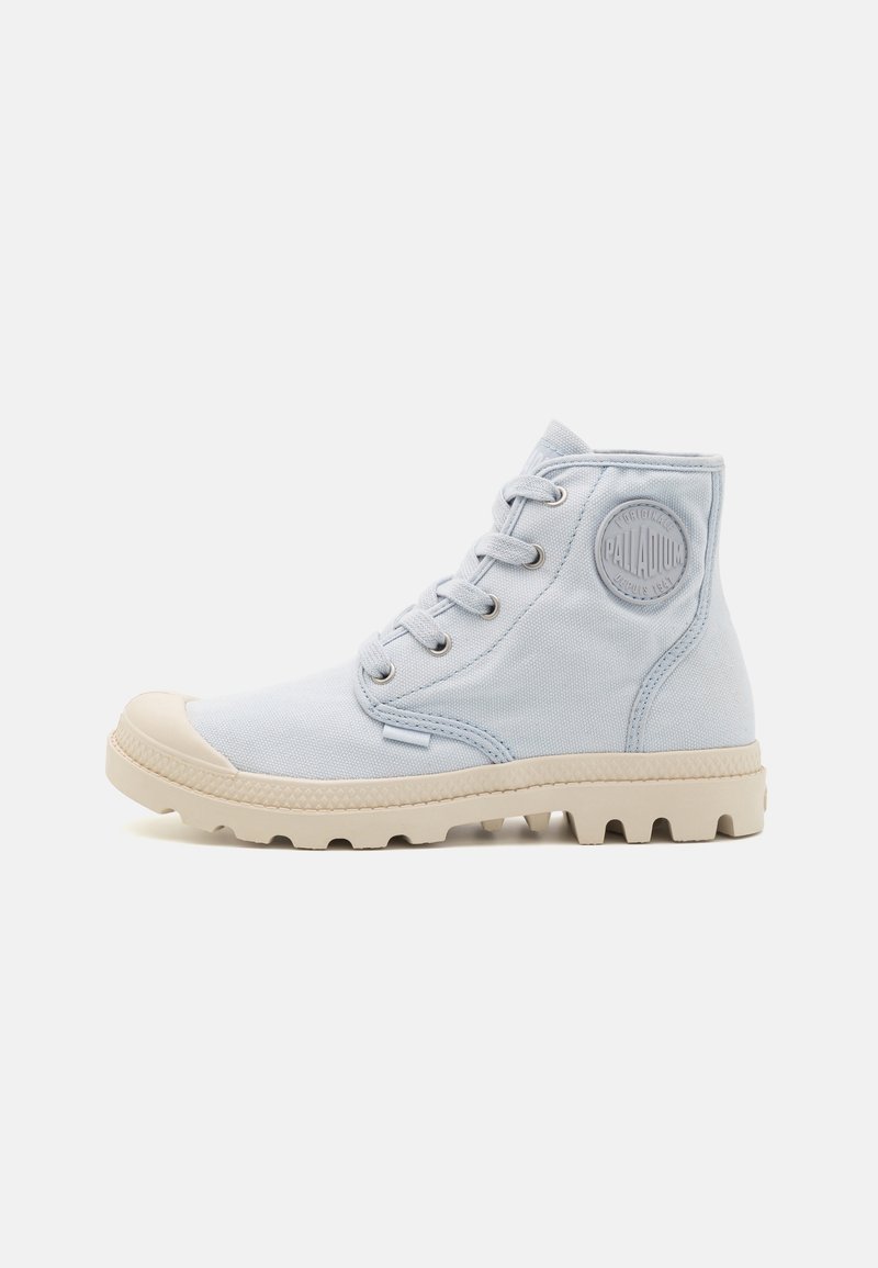 Chaussure montante en toile bleu clair avec bout rond, semelle extérieure en caoutchouc blanche, coutures visibles et patch de logo en relief sur le côté.