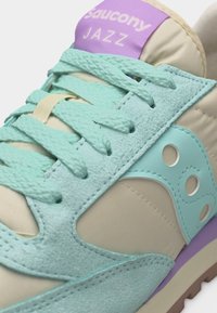 Παγωμένο πράσινο και μπεζ αθλητικό παπούτσι Saucony Jazz με πάνελ από σουέτ και ύφασμα, κορδόνια σε παγωμένη απόχρωση και μωβ ετικέτα στη γλώσσα.