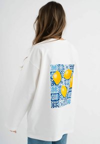 Witte sweatshirt met een relaxte pasvorm, voorzien van een blauw-wit patroon met drie gele citroenen gedrukt op de achterkant.