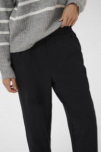 Pantalons noirs avec une texture lisse et une taille élastique, associés à un pull rayé gris et blanc. Détails de boutons et de poches visibles.