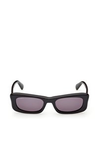 Lunettes de soleil rectangulaires noires avec des montures épaisses et des verres teintés foncés, posées sur une surface blanche.