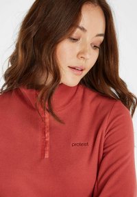 Langærmet, koralfleece pullover med halvhøj krave og kvart lynlås. Har et lille logo i kontrastfarve på brystet.