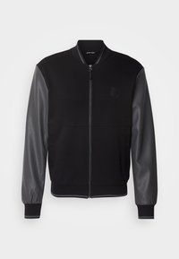 Veste bomber noire avec une fermeture éclair sur le devant, col, poignets et ourlet en maille côtelée, et manches en cuir gris foncé contrastantes.