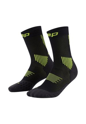 Schwarze Sportsocken mit grünen Akzenten, ausgestattet mit einem strukturierten Muster und einem unterstützenden Design. Die Socken haben verstärkte Zehen und Fersen.