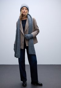 Beżowa marynarka, niebieski dzianinowy szalik, pasująca czapka, szary top, ciemne jeansy wide-leg i czarne botki za kostkę. Miękkie faktury i warstwowy design.
