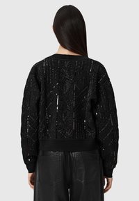 Czarny pikowany sweatshirt z cekinowymi wzorami florystycznymi i geometrycznymi, z prążkowanymi mankietami i dołem, noszony z czarnymi skórzanymi spodniami.