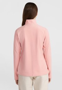 Light pink fleece jacket with a high collar, long sleeves, and a soft texture. Features a curved hem at the bottom for a relaxed fit.