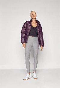 Vetrová bunda tmavofialovej farby s lesklým povrchom, doplnená o sivé legíny a biele tenisky. Minimalistický dizajn, skrátený strih.