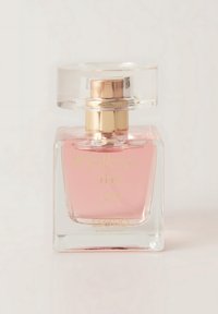 Szklana butelka na perfumy w kształcie kwadratu, przezroczysta podstawa, jasnoróżowy płyn i korek wykończony złotem. Tekst brzmi „#podążaj za radością.”