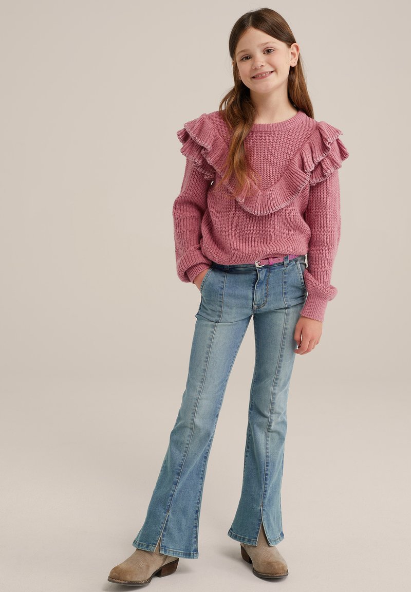 Rosa stickad tröja med volangaxlar, i kombination med ljusblå utsvängda jeans med sidofickor och beige ankelstövlar.